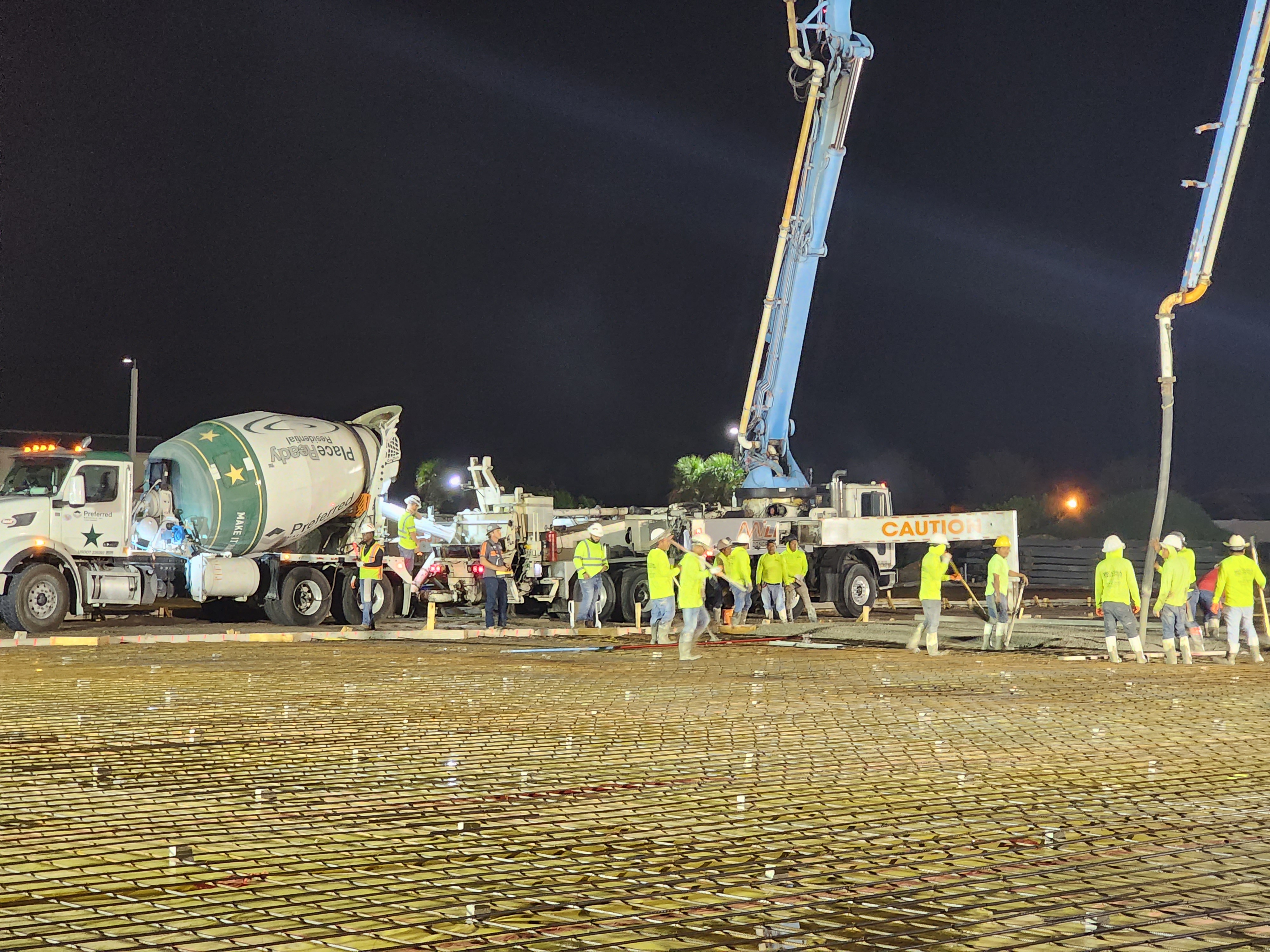Night concrete pour with a crew, pump truck, and finishers on the slab